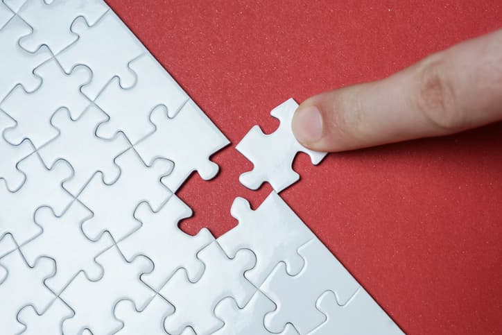 Hand putting piece of white jigsaw puzzle on red background