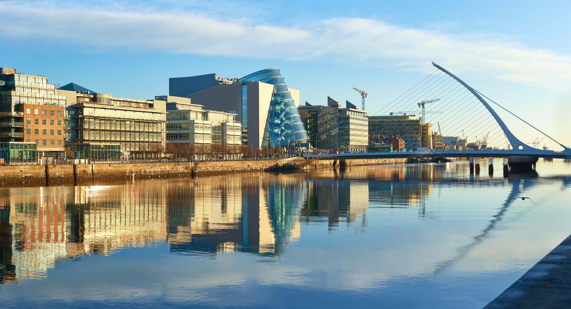 Modern buildings and offices on Liffey river in Dublin on a bright sunny day. Bridge on the right is a famous Harp bridge.