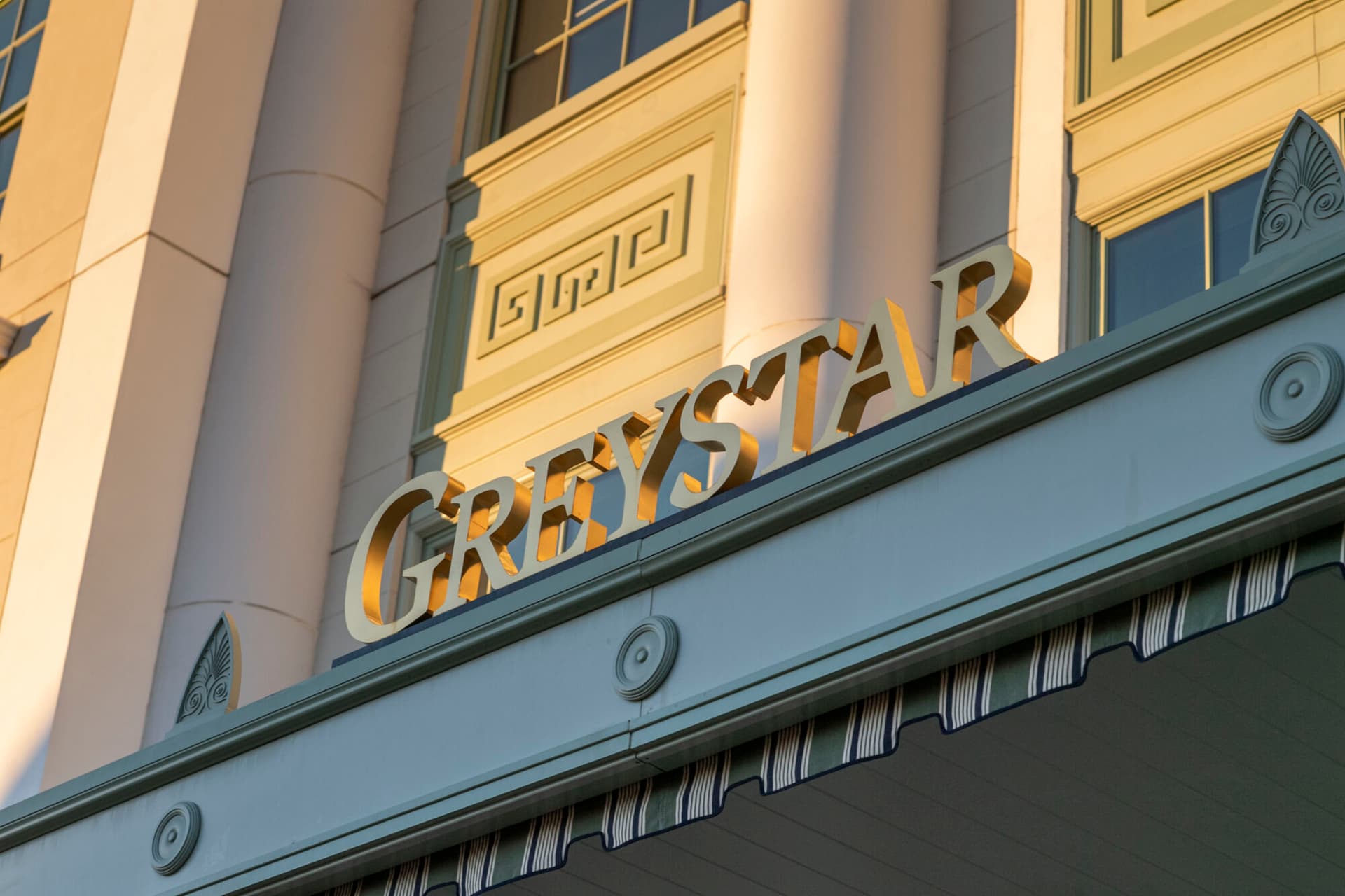 Greystar's logo on the facade of its office, illuminated by sunlight at sunset.