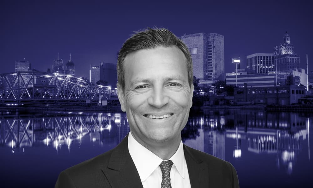 A portrait of PGIM Real Estate's John Jacobs transposed on a navy blue-tinted landscape image of Newark, New Jersey.