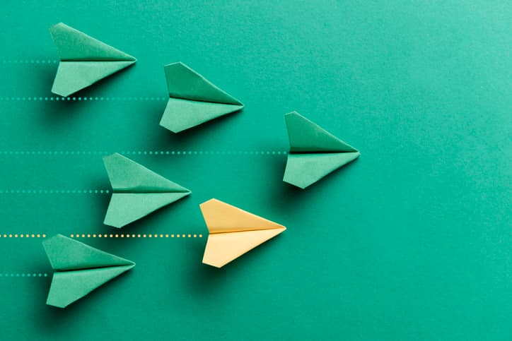 One yellow paper plane is flying on green background among a group of green paper planes. Representing individuality.