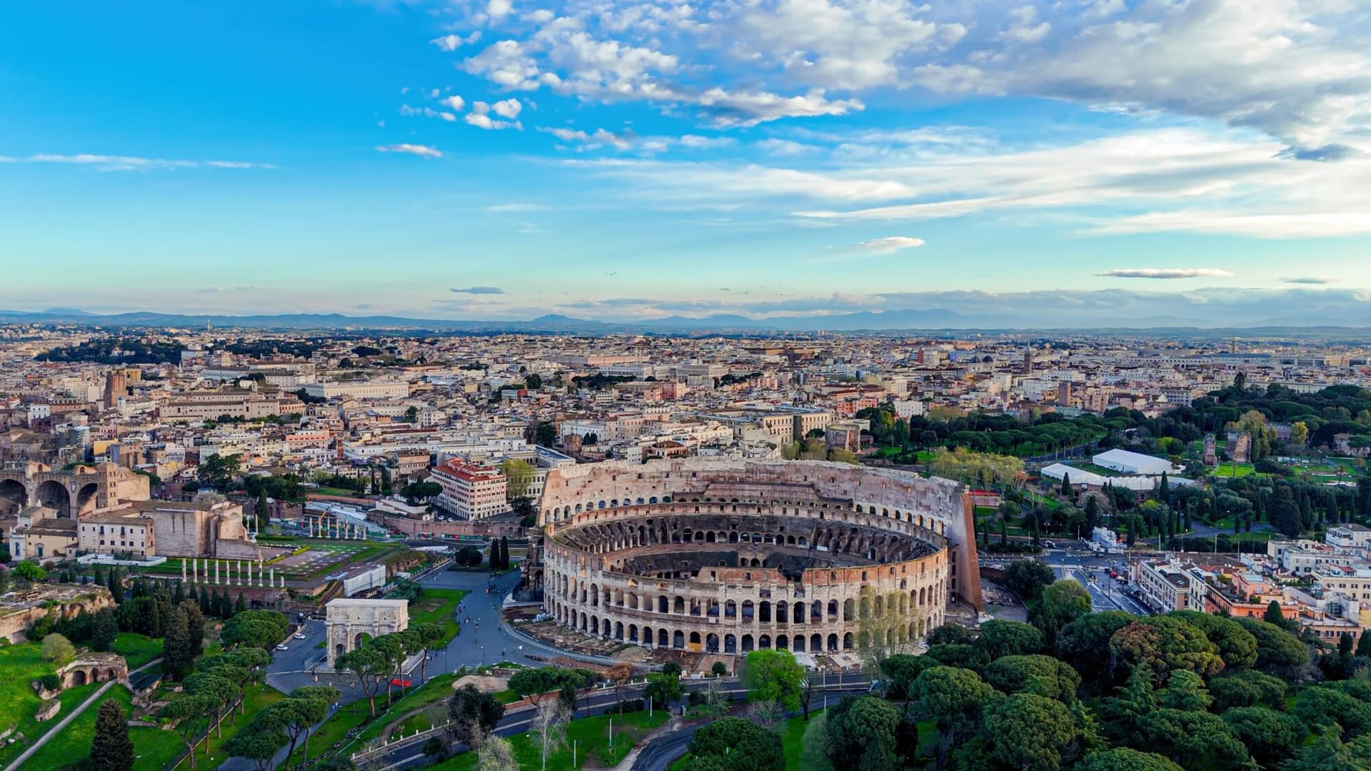 This photo captures dynamic aerial footage of the Colosseum in Rome, Italy, emphasizing its circular form, layered stone arches, and the surrounding historic urban landscape. Sweeping shots transition from wide panoramic views of the Roman cityscape to dramatic close-ups of the Colosseum’s interior chambers, showcasing its grand scale and architectural complexity. As one of the most recognizable landmarks of the Roman Empire, this amphitheater stands as a symbol of classical heritage and historical significance, making the footage ideal for documentaries, travel features, or educational media.